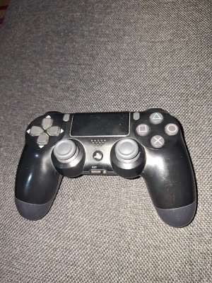 Svart DualShock 4 handkontroll PS4 - Säljer en svart DualShock 4 handkontroll från Sony till PlayStation 4. Den har en klassisk design med touchpad, två analoga spakar, styrkors och de ikoniska PlayStation-knapparna. Tillverkad i plast med matta och blanka ytor. Perfekt för gaming och multiplayer.