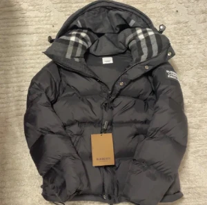 Svart dunjacka från Burberry - Svart dunjacka från Burberry med avtagbara ärmar, så du kan bära den som väst. Bästa priserna här på Plick och skicka gärna in bud då jag kan sänka priset vid snabb affär.