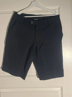 Mörkblå shorts från Abacus - Snygga mörkblå shorts från Abacus med klassisk passform. Shortsen har två sidofickor fram och två bakfickor, samt bälteshällor och knappstängning. Perfekta för sommardagar och sportiga aktiviteter.