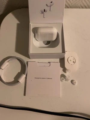 Apple AirPods Pro med laddningsetui - Säljer ett par vita Apple AirPods Pro med trådlöst laddningsetui. Hörlurarna har silikonproppar i olika storlekar, brusreducering och levereras med originalförpackning, laddkabel och manual. Snygg och stilren design i plast, perfekt för musik och samtal.