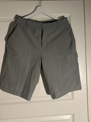 Gråa klassiska shorts med fickor - Snygga grå shorts med normal passform och bälteshällor. De har två sidofickor fram och två passpoalfickor bak. Perfekta för sommaren och tillverkade i ett mjukt, lätt material som känns bekvämt hela dagen.