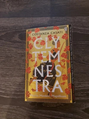 Clytemnestra av Costanza Casati - En roman med gul och orange omslag, dekorerad med röda löv och antika mönster. Boken handlar om Clytemnestra, en mytisk drottning, och utforskar teman som hämnd, styrka och makt i antikens Grekland. Perfekt för dig som gillar episka berättelser och starka kvinnliga huvudpersoner.