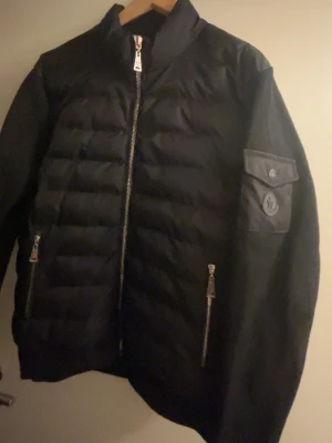 Svart cardiganjacka från Moncler - Snygg svart cardiganjacka från Moncler med quiltad front och släta ärmar. Jackan har dragkedja framtill, två fickor med dragkedja och en ficka med lock och Moncler-logga på ärmen. Materialmix med vadderad front och mjuka ärmar ger en modern look.
