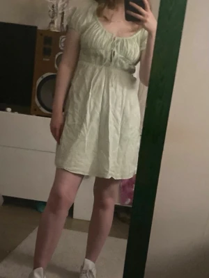 Mint grön kort klänning med snörning - Söt ljusgrön kort klänning med snörning framtill och puffiga kortärmar. Klänningen har en lätt rynkad överdel och är tillverkad i ett tunt, mjukt material som passar perfekt för varmare dagar.Skrynklig bara att stryka.