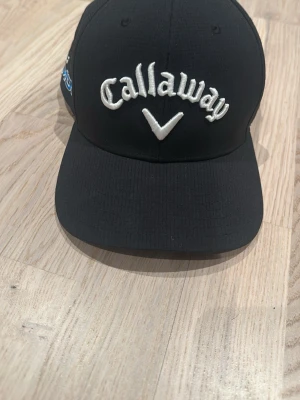 Callaway keps med brodyr - Snygg mörkblå keps från Callaway med vit broderad logga framtill och texten 'CHROME TOUR' på sidan. Klassisk böjd skärm och justerbar passform. Perfekt accessoar för golf eller streetwear. Tillverkad i ett slitstarkt tygmaterial.
