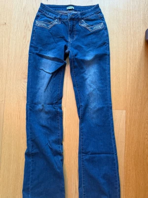 Blå bootcut jeans med broderi - Snygga blå bootcut jeans från Madlady med  broderade fickor bak och dekorativa detaljer fram. Jeansen har låg midja och är gjorda i ett mjukt denimtyg med stretch. Oanvända.