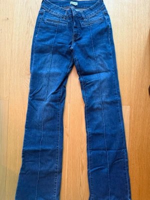 Blå bootcut jeans med broderade fickor - Snygga blå bootcut jeans från madlady. Pyret med dekorativa sömmar framtill och broderade bakfickor med knappar. 