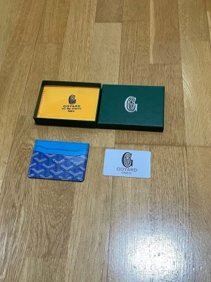 Blå korthållare  - Snygg blå korthållare med det klassiska mönstret i vitt och grått. Tillverkad i canvas och läder, perfekt för kort och ID. Kommer med originalask och certifikat. En stilren accessoar för dig som gillar exklusiva detaljer.