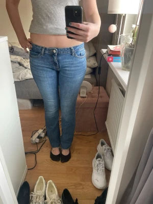 Blå raka jeans med låg midja - Säljer ett par klassiska blå jeans med låg midja och raka ben. Jeansen har fem fickor och stängs med dragkedja och knapp. Perfekta till vardags och lätta att matcha med olika toppar.