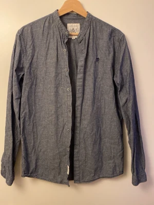Grå henley-skjorta  - Snygg grå henley-skjorta med lång ärm och knappar framtill. Skjortan har en enkel och stilren design med liten broderad logga på bröstet. Perfekt för en avslappnad men ändå uppklädd look. Knappt använd. Mycket bra skick och fortfarande väldigt snygg. 