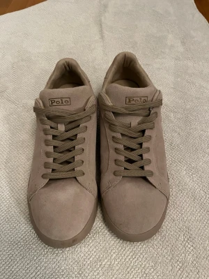 Beige sneakers från Polo Ralph Lauren - Snygga beige sneakers från Polo Ralph Lauren i mockaimitation. Klassisk låg modell med matchande beige snörning  de är oanvända och nypris är 1800 men jag säljer för 800