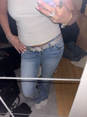 Glittrigt silverbälte med strass - Säljer ett glittrigt bälte i silver med massor av strassdetaljer som verkligen fångar ljuset. Bältet har klassisk form och justerbart spänne, perfekt för att ge extra bling till jeans eller kjol. Riktigt snygg accessoar för dig som vill sticka ut.