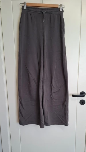Grå mjukisbyxor från H&M - Säljer ett par grå mjukisbyxor från H&M med breda ben och dragsko i midjan. Byxorna är tillverkade i mjukt och bekvämt material, perfekta för chill dagar. Klassisk design utan tryck eller detaljer, passar till allt.