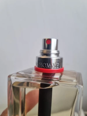Dior Homme parfymflaska - Snygg parfymflaska från Dior Homme med stilren, fyrkantig design i genomskinligt glas. Flaskan har en silverfärgad spraydel med röd detalj och tydlig Dior Homme-gravyr. Perfekt för dig som gillar exklusiva dofter och modern design.