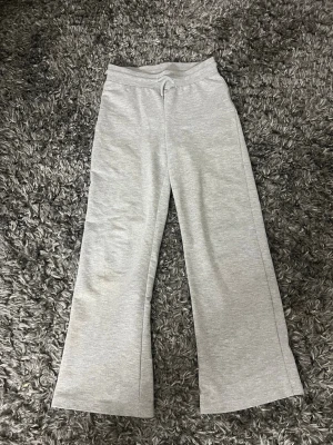 Grå mjukisbyxor med raka ben - Säljer ett par ljusgrå mjukisbyxor med raka, vida ben och resår i midjan med dragsko. Byxorna är tillverkade i mjukt sweatshirtmaterial som känns skönt mot huden. Perfekta för chill dagar hemma eller när du vill ha en avslappnad look.