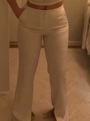 Vita högmidjade byxor i mjukt tyg - Säljer ett par vita kostymbyxor med rak passform. Byxorna är i ett mjukt och stretchigt material som sitter snyggt och bekvämt. Perfekta för dig som gillar en clean och stilren look. Den är aldrig använd. 