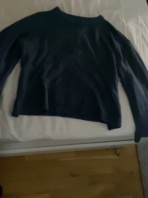 Mörkblå stickad tröja - En enkel och stilren mörkblå stickad tröja med rund hals och långa ärmar. Tröjan har en rak passform och är mjuk i materialet, perfekt för kyliga dagar. Passar till både jeans och kjol för en avslappnad look.