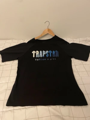 Svart Trapstar t-shirt med tryck - Snygg svart t-shirt från Trapstar med stort tryck i vitt och blått på bröstet där det står 'Trapstar It's a secret'. Klassisk passform och korta ärmar, perfekt till streetwear-stilen. Priset kan diskuteras 