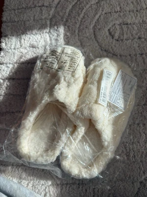 Mjuka vit/beige fluffiga tofflor - Säljer ett par supermysiga vita tofflor med fluffig och mjuk yta. Perfekta att glida runt i hemma när du vill ha det extra bekvämt. Tofflorna har en enkel slip-in design och är tillverkade i ett gosigt syntetmaterial. små i storlek 