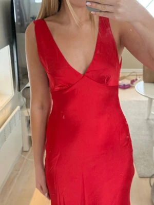 Röd långklänning med v-ringning - Säljer denna supersnygga balklänning då den tyvärr var för kort på mig! Superskönt material i satin och öppen rygg🥰 Jag är 171cm och den var typ 5cm för kort om jag skulle haft klackar till tyvärr…