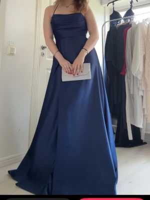 Marinblå långklänning med snörning - Snygg marinblå långklänning med smala axelband och öppen rygg med dekorativ snörning. Klänningen har en elegant, figurnära överdel och ett svepande, utsvängt kjolparti. Perfekt för dig som ska på bal!💕Nypris 2700kr