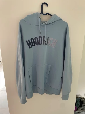 Ljusblå hoodie från Hoodrich - Snygg ljusblå hoodie från Hoodrich med broderad logga i svart och vitt på bröstet. Hoodien har stor huva med dragsko, magficka och ribbade muddar vid ärmar och nederkant. Perfekt för en chill och avslappnad stil.