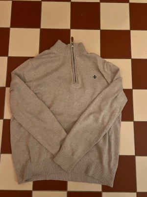  Morris tröja halvzip - Säljer en beige Morris tröja med halvzip och hög krage. Tröjan har ribbade muddar vid ärmslut och nederkant samt en liten broderad logga på bröstet. Perfekt för lager på lager och riktigt skön att ha på sig.