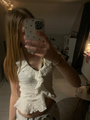 Vit volangblus  - Supersöt vit blus med smockad struktur och volangdetaljer framtill. Med en lätt croppad passform i storlek xs från Nelly 