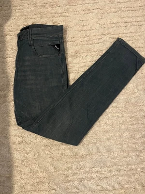 Mörk grå slim fit jeans från replay - Snygga grå slim fit jeans från replay med klassisk femficksdesign och diskreta slitningar. Jeansen har normal midja och raka ben, tillverkade i mjukt denimtyg som ger en bekväm känsla. Perfekta för dig som gillar en stilren och enkel look.