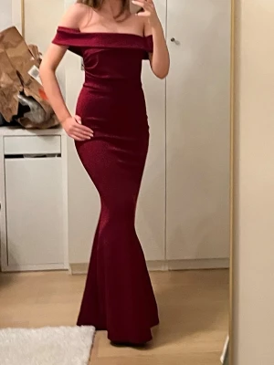 Vinröd offshoulder långklänning - Elegant vinröd långklänning med offshoulder-design och figurnära passform. Klänningen är nyinköpt och aldrig använd (prislappen är kvar). Köpt på Zalando och är från märket WalG. Perfekt för bal eller festliga tillfällen. Materialet känns mjukt och rejält. Känns som det är bra kvalitet och inte tunt och billigt. 