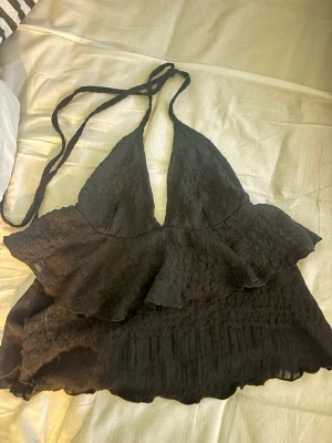 Svart volang topp med knyt - Säljer en svart halterneck topp med volangdetaljer och knyt i nacken från Nelly i mycket bra skick💞