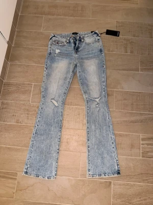Ljusblå bootcut jeans True Religion - Säljer ett par ljusblå bootcut jeans från True Religion med slitningar på benen och klassiska broderade bakfickor. Jeansen har en tvättad look och är tillverkade i denim med dragkedja och knapp framtill. Perfekta för en avslappnad och trendig stil.