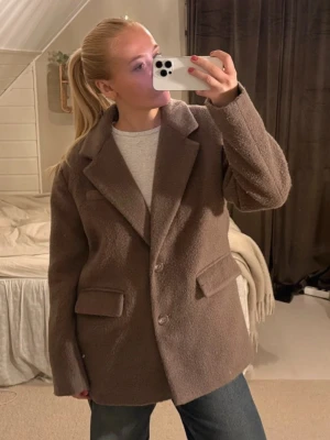 Brun kappa - Säljer en brun kappa med två knappar framtill och breda slag. Kappan har två stora fickor med lock och är i storlek S, lite oversized. Perfekt för att hålla sig varm under kyliga dagar.