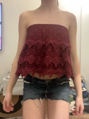 Vinröd axelbandslös topp med spets  - Säljer en vinröd axelbandslös tubtopp med flera lager spets och dekorativa detaljer. Kan ha den som både topp och kjol, köpt från sellpy och är i bra skick, storlek S