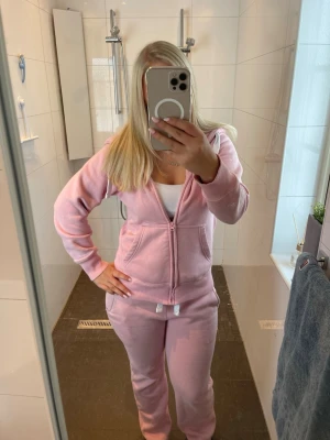 Rosa mysig loungewear-set med hoodie - Säljer ett rosa loungewear-set med mjuk hoodie och matchande byxor. Hoodien har dragkedja, fickor och snören vid huvan. Byxorna har resår i midjan och raka ben. Perfekt för chill hemma eller när du vill vara bekväm. Materialet är fleeceliknande och riktigt mjukt.