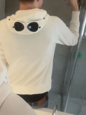 Vit zip hoodie från C.P. Company KVITTO FINNS FRÅN NK - Säljer en vit hoodie från C.P. Company med dragkedja framtill och klassiska goggles på huvan. Hoodien har fickor på sidorna och ribbade muddar vid ärmslut och nederkant. Perfekt för dig som gillar streetwear och vill sticka ut. Köpt på NK i Stockholm, kvitto finns!🤩