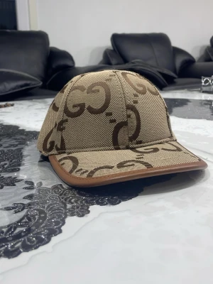 Beige keps från Gucci med GG-mönster - Säljer en beige keps från Gucci med det klassiska GG-mönstret i brunt. Kepsen har böjd skärm med brun kant och justerbart band bak. Tillverkad i canvasmaterial som ger en exklusiv känsla och streetwear-vibe.