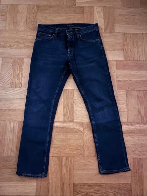 Mörkblå nudie jeans - Snygga mörkblå jeans med rak passform och klassisk femficksdesign. Jeansen har kontrastsömmar och normal midja. Tillverkade i denim med en stilren look som passar till det mesta. Perfekta för dig som gillar en enkel och tidlös stil.