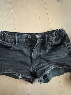 Svarta jeansshorts med rå kant - Snygga svarta jeansshorts med rå, fransig kant och klassisk femficksdesign. Shortsen har knapp och dragkedja framtill samt bälteshällor. Perfekta för en avslappnad och trendig look. De är tyvärr för små för mig! 