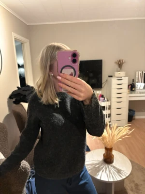 Mörkgrå stickad tröja - Mysig mörkgrå stickad tröja med rund hals och långa ärmar. Tröjan har en enkel och klassisk design som passar perfekt till jeans eller mjukisbyxor. Materialet ser ut att vara ull eller en ullblandning för extra värme.