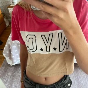 NYC Topp från Lager 157 - Säljer en magtröja från Lager 157 med NYC-tryck framtill. Toppen har blockfärger i rosa, vitt och beige, korta ärmar och rund halsringning. Perfekt för dig som gillar streetstyle och vill ha en chill vibe på outfiten. Den är i bra skick kanske använd 2 gånger. Står att den är i stl 160 men passar mig som har xs-s. Pris går att diskutera. Hör av er om frågor!❤️(Säljer även på Vinted ifall man skulle vilja köpa där)