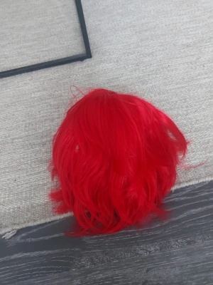 Röd cosplayperuk med korta lager - Säljer en intensivt röd peruk med korta, lagerklippta strån. Perfekt för maskerad eller cosplay, och ger ett riktigt färgstarkt intryck. Peruken är syntetisk och har en naturlig volym. Passar dig som vill sticka ut på nästa event!