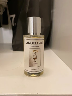 ANGELI 23.0 parfym - ANGELI 23.0 extrait de parfum från one bold chemist. Flaskan är cylindrisk i genomskinligt glas med silverfärgad spraykork. Etiketten har en konstnärlig illustration och tydlig text. Innehållet är ljusgult och flaskan har en modern, minimalistisk design.