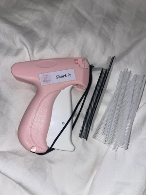 Short it uf - Short it erbjuder en enkel och snabb lösning för att justera byxlängden utan att sy. Med en smidig häftpistol kan användaren fästa och anpassa byxor på sekunder, oavsett material. Häftmaterialet är lätt att ta bort utan att lämna märken, och påfyllning av häftmaterial ingår.