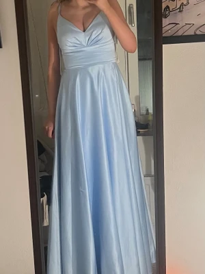 Ljusblå balklänning - Superfin ljusblå långklänning i glansigt satinmaterial. Endast använd 1 gång, den har en liten fläck (se bild 2) men det är inget som märks! Storleken är specifik för det här märket jag uppskattar att den motsvarar S-M. Skriv gärna till mig om du vill ha exakta mått! 