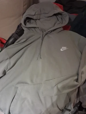 Grön hoodie från Nike med logga - Säljer en stilren grön hoodie från Nike med klassisk vit logga på bröstet. Hoodien har en stor huva med dragsko och en rymlig magficka. Perfekt för dig som gillar en enkel och clean look. Materialet känns mjukt och bekvämt.