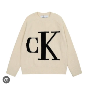 Beige stickad tröja från Calvin Klein - Säljer en beige stickad tröja från Calvin Klein med stor svart CK-logga framtill. Tröjan har rund halsringning, långa ärmar och är gjord i mjukt stickat material. Perfekt för dig som gillar enkel men snygg design.
