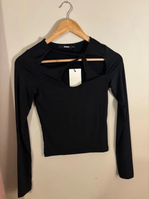 Svart topp med cut out - Trendig svart topp från Bik Bok med långa ärmar och cool cut out-detalj framtill. Figurnära passform och mjukt stretchigt material som känns skönt mot huden