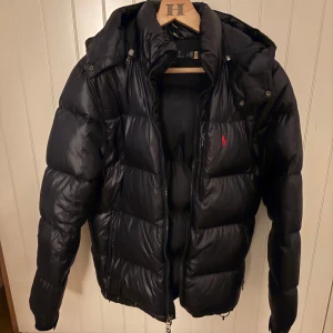 Mörkblå dunjacka från Polo Ralph Lauren - Säljer en mörkblå pufferjacka från Polo Ralph Lauren med huva och dragkedja. Använt någon gång men ser och känns helt ny. Säljer för 2199kr men priset kan diskuteras. Nypris 6000kr