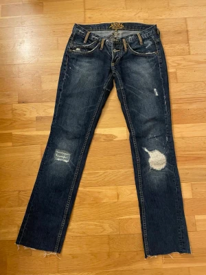 Mörkblå jeans från F.T. Porter - Säljer ett par mörkblå jeans från F.T. Porter med slitna detaljer, råa benslut och broderade bakfickor. Jeansen har kontrastsömmar, dekorativa knappar och patch på linningen.        Ni får gärna be om exakta mått eller fler bilder, så hjälper jag gärna till🤗Byxorna endast använda fåtal gånger men saknar tyvärr en knapp (påverkar/syns inget när man har på sig dem)😊Priset kan diskuteras 💕Skicka gärna om eventuella frågor!!💕